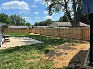 Long wood privacy fence enclosing a residential backyard with a patio and lawn